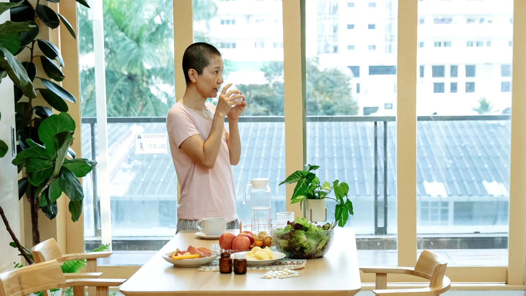 Woman in a pale pink shirt drinking a glass of water at home – WhiteLine Dental Clinic Al Rigga